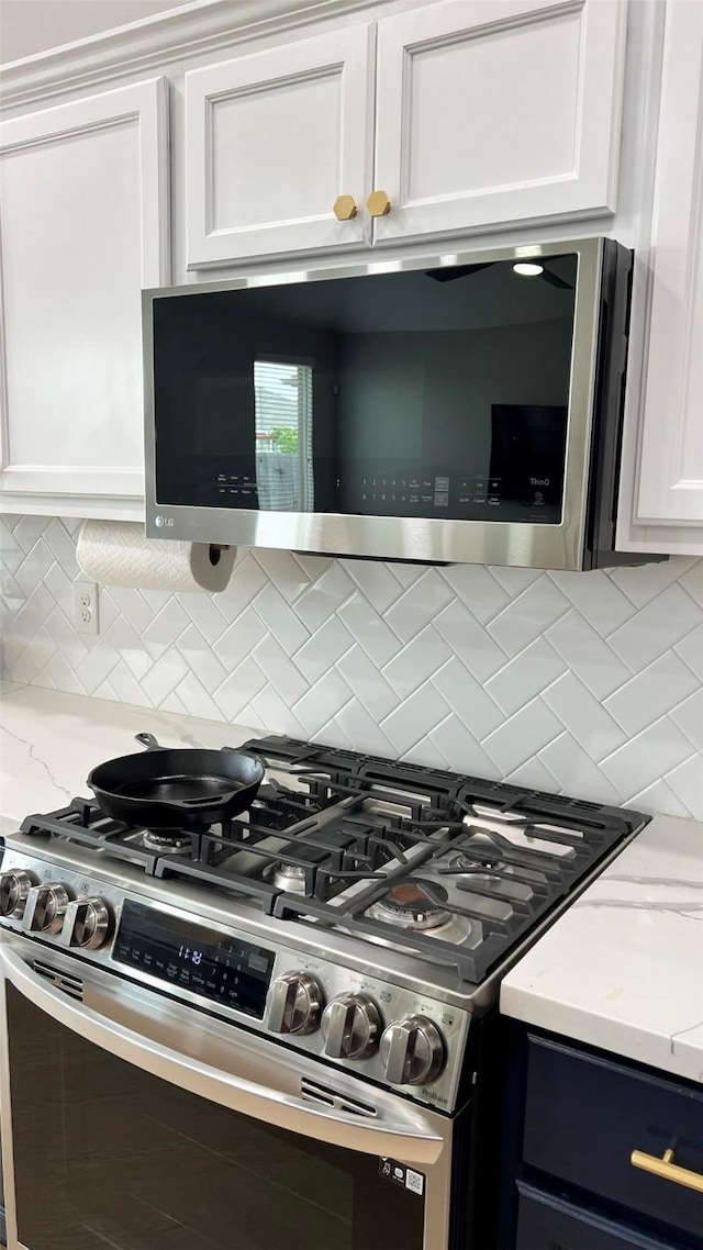 kitchen featuring appliances with stainless steel finishes, white cabinetry, light stone counters, and decorative backsplash