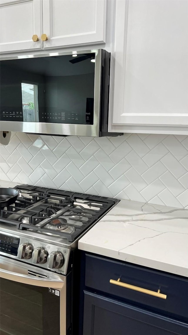 kitchen with appliances with stainless steel finishes, white cabinets, light stone counters, and tasteful backsplash