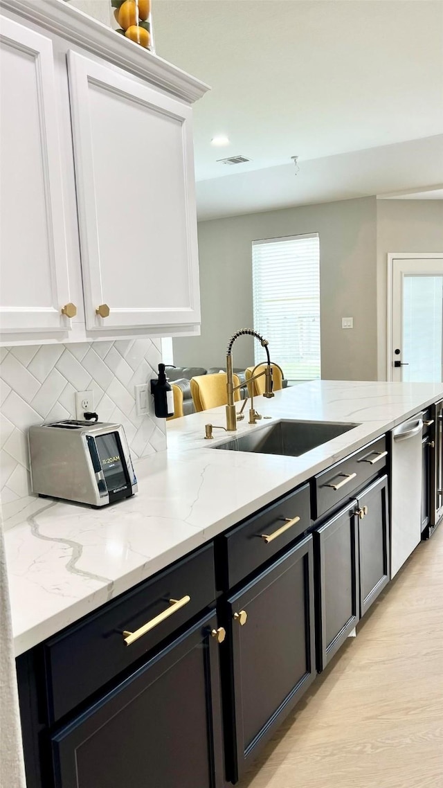 kitchen with white cabinets, decorative backsplash, light stone countertops, and sink