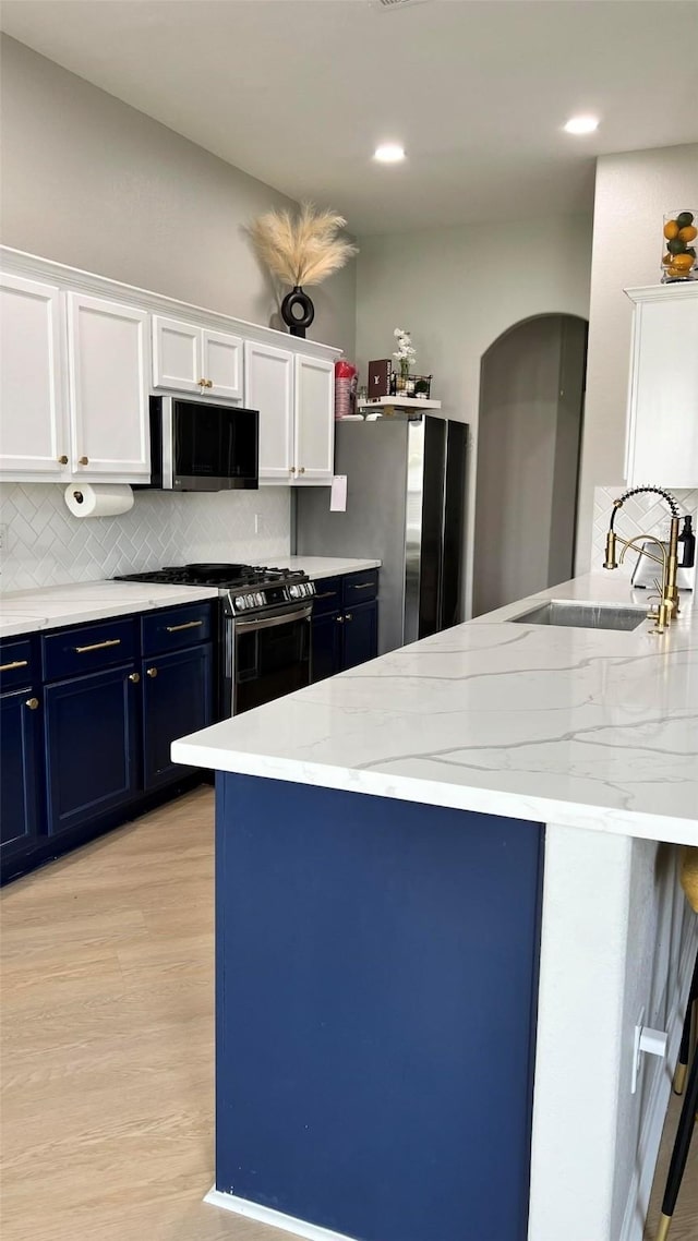 kitchen featuring stainless steel appliances, sink, white cabinets, light hardwood / wood-style floors, and tasteful backsplash