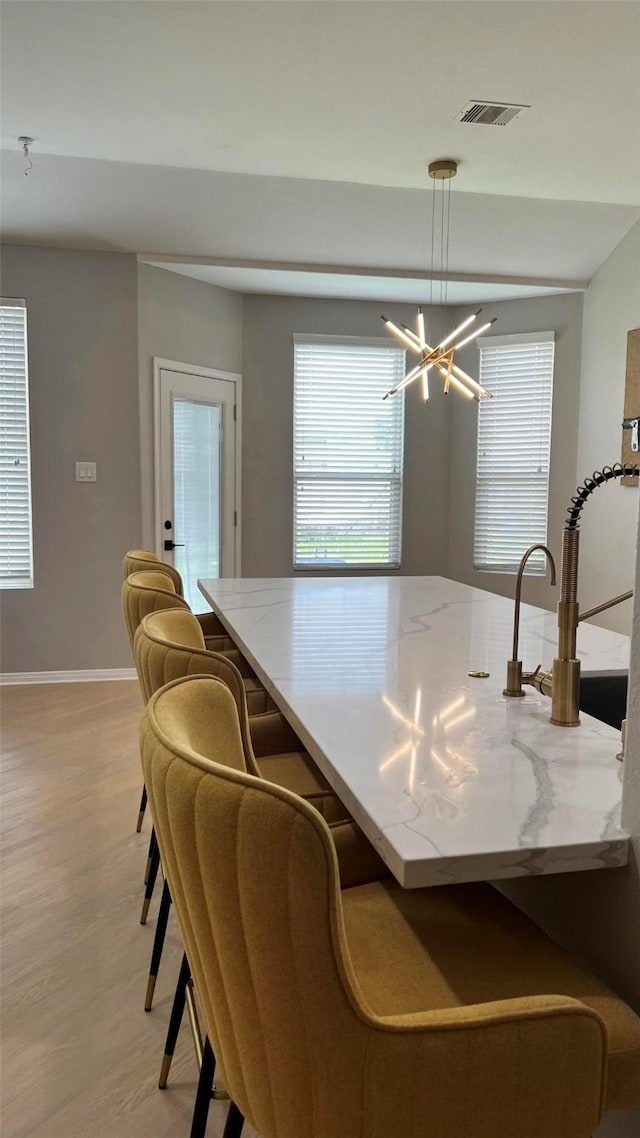 kitchen with light wood-type flooring, decorative light fixtures, an inviting chandelier, and light stone countertops