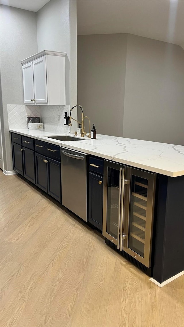 kitchen with sink, white cabinetry, light wood-type flooring, tasteful backsplash, and stainless steel dishwasher