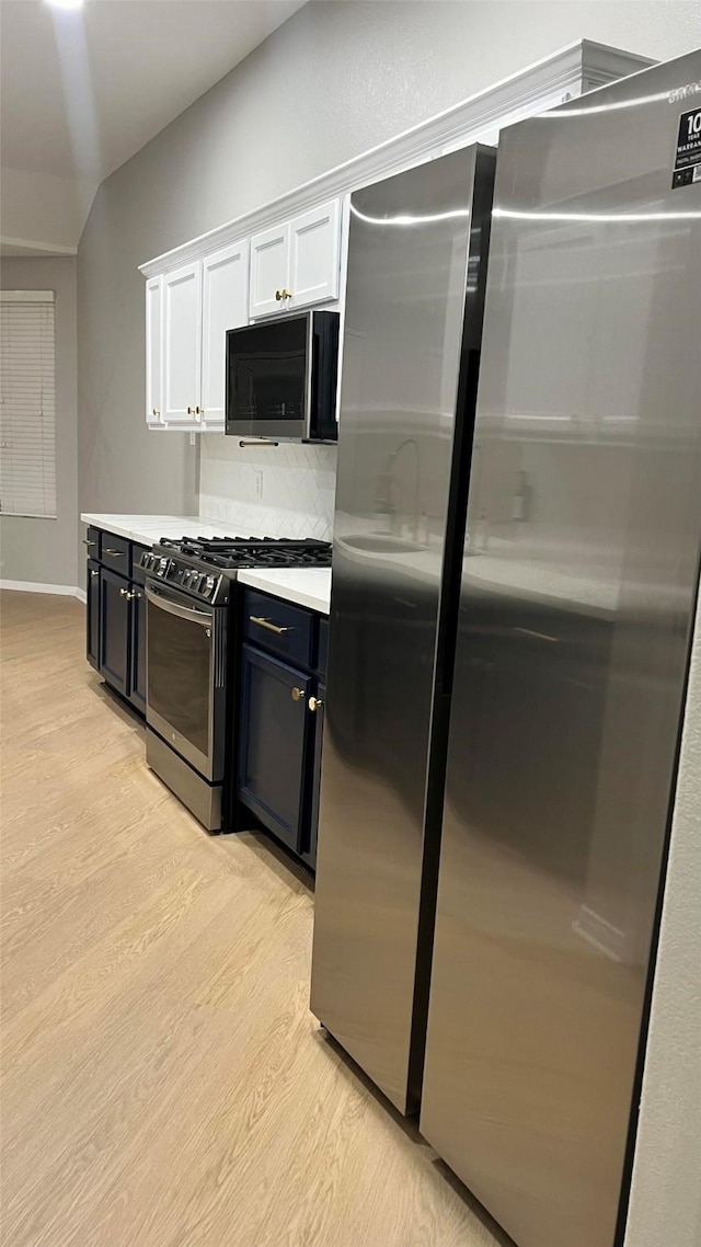 kitchen featuring white cabinetry, vaulted ceiling, appliances with stainless steel finishes, decorative backsplash, and light hardwood / wood-style flooring