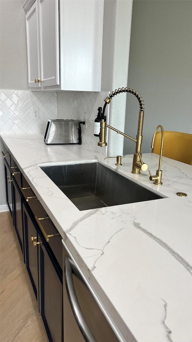 kitchen with light stone counters, white cabinets, backsplash, and sink