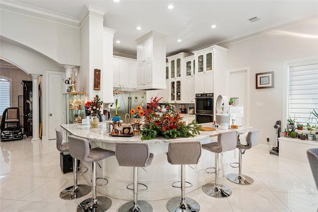 kitchen featuring built in refrigerator, white cabinetry, multiple ovens, decorative columns, and ornamental molding