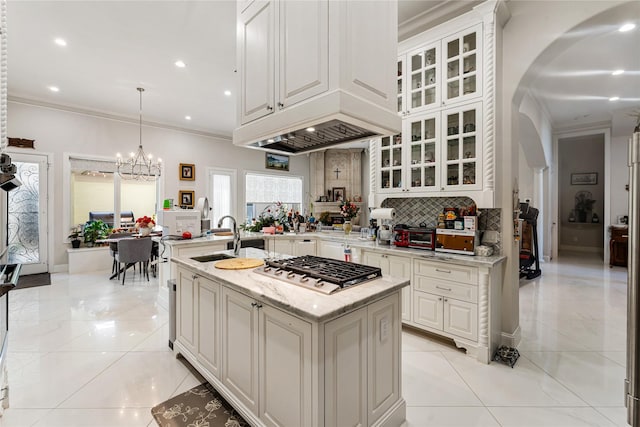 kitchen featuring sink, crown molding, light stone counters, a center island with sink, and stainless steel gas stovetop