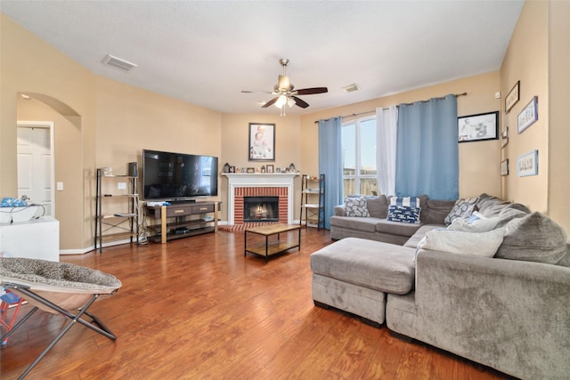 living room featuring ceiling fan, hardwood / wood-style floors, and a brick fireplace