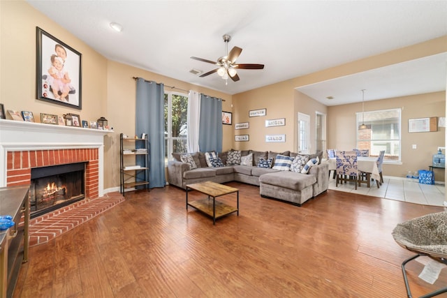 living room featuring hardwood / wood-style flooring, a brick fireplace, and ceiling fan