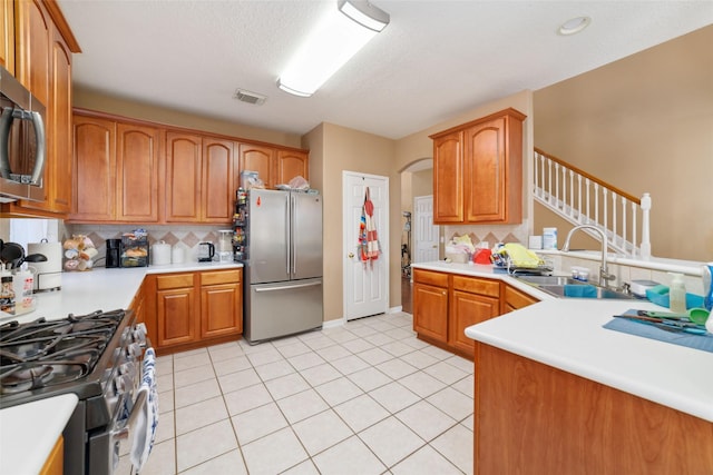 kitchen with decorative backsplash, a textured ceiling, stainless steel appliances, sink, and light tile patterned flooring