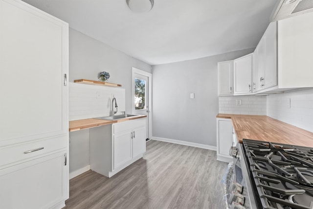 kitchen with wooden counters, sink, light hardwood / wood-style flooring, stainless steel gas stove, and white cabinetry