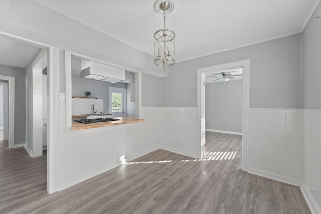 unfurnished dining area featuring hardwood / wood-style floors, ceiling fan with notable chandelier, and ornamental molding