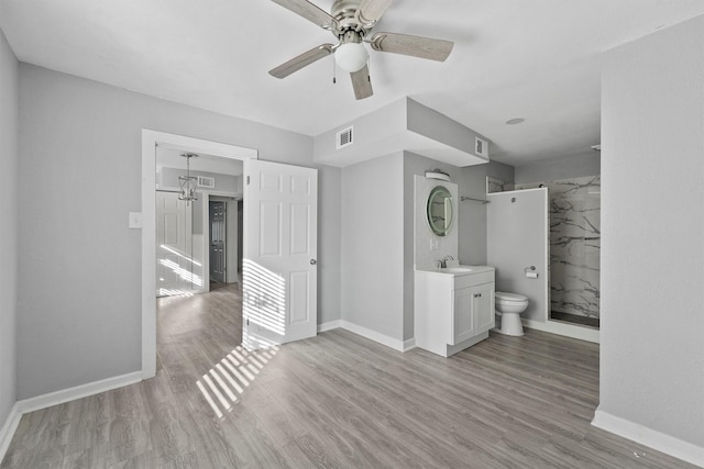 interior space featuring a tile shower, ceiling fan, hardwood / wood-style floors, toilet, and vanity