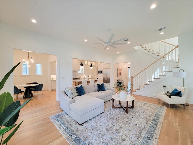 living room featuring hardwood / wood-style floors, crown molding, and ceiling fan with notable chandelier