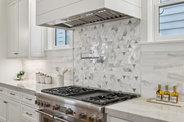 kitchen with tasteful backsplash, stainless steel range, light stone countertops, white cabinets, and wall chimney exhaust hood