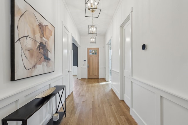 hallway with crown molding, an inviting chandelier, and light hardwood / wood-style flooring