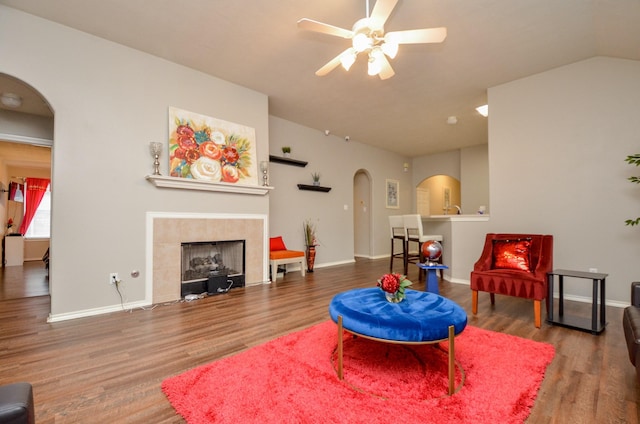 living room with a tile fireplace, wood-type flooring, vaulted ceiling, and ceiling fan