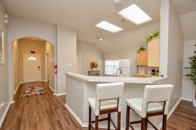 kitchen featuring kitchen peninsula, vaulted ceiling, dark wood-type flooring, light brown cabinets, and white fridge