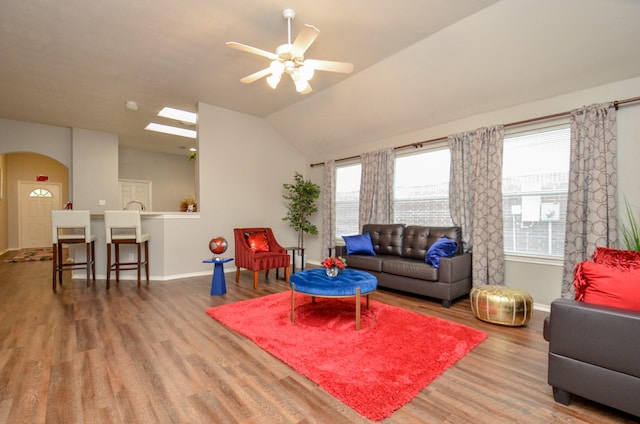 living room featuring ceiling fan, vaulted ceiling with skylight, and hardwood / wood-style flooring