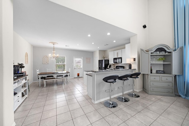 kitchen with an inviting chandelier, white cabinets, black appliances, light tile patterned floors, and kitchen peninsula