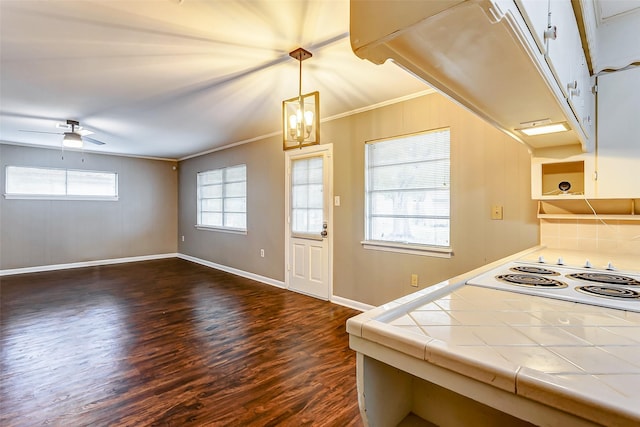 kitchen featuring tile counters, a healthy amount of sunlight, white stovetop, crown molding, and decorative light fixtures