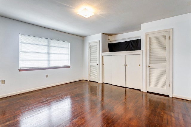 unfurnished bedroom with dark hardwood / wood-style flooring and two closets