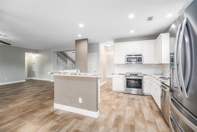 kitchen with a center island, light stone counters, decorative backsplash, white cabinets, and appliances with stainless steel finishes