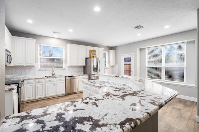 kitchen with a large island, white cabinets, light stone countertops, and appliances with stainless steel finishes