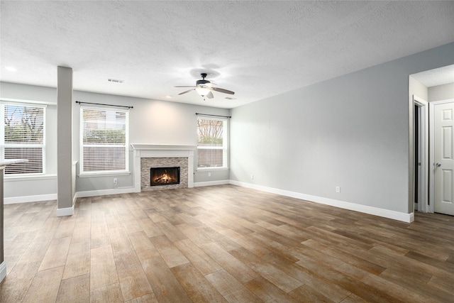 unfurnished living room featuring wood-type flooring, a textured ceiling, a stone fireplace, and ceiling fan