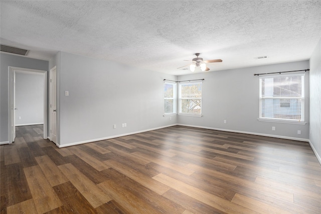 empty room with a textured ceiling, ceiling fan, a healthy amount of sunlight, and dark hardwood / wood-style floors