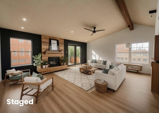 living room with light hardwood / wood-style flooring, ceiling fan, lofted ceiling with beams, a large fireplace, and wood walls