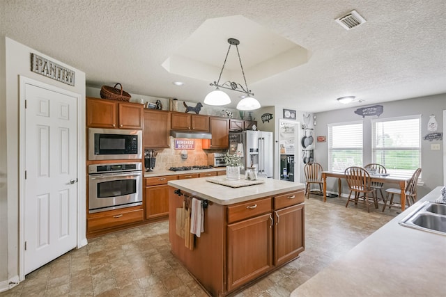 kitchen featuring decorative backsplash, stainless steel appliances, a raised ceiling, pendant lighting, and a kitchen island