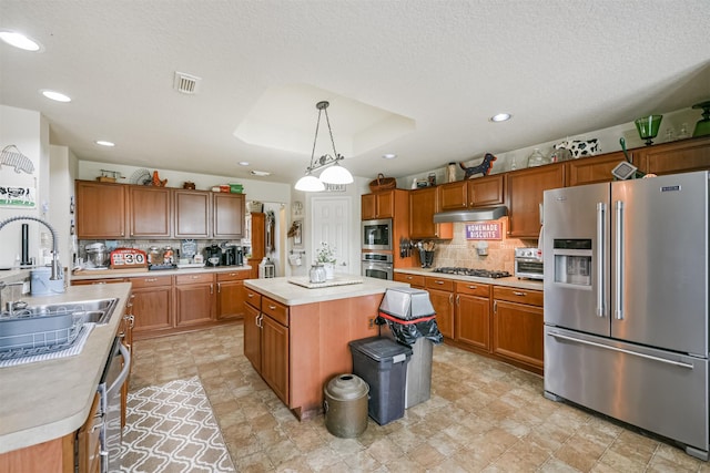 kitchen featuring backsplash, a textured ceiling, appliances with stainless steel finishes, decorative light fixtures, and a kitchen island