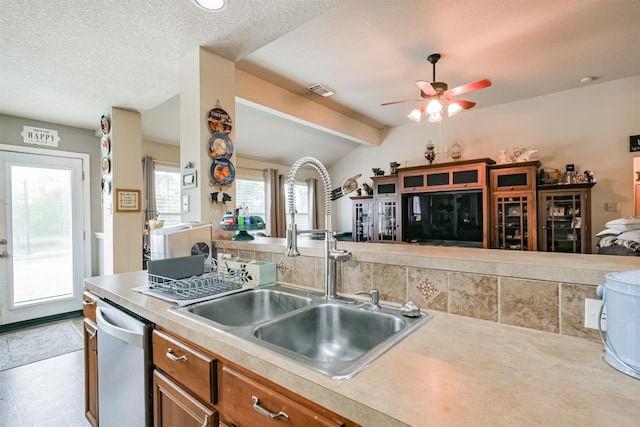 kitchen with ceiling fan, sink, vaulted ceiling with beams, stainless steel dishwasher, and a textured ceiling