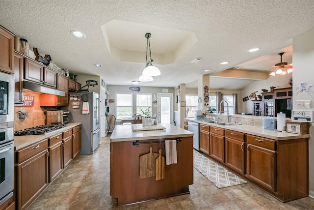 kitchen featuring appliances with stainless steel finishes, a textured ceiling, sink, decorative light fixtures, and a kitchen island