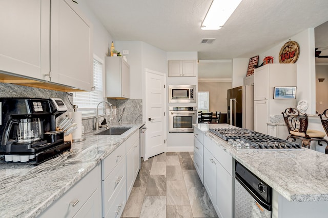 kitchen featuring white cabinets, sink, a textured ceiling, light stone counters, and stainless steel appliances