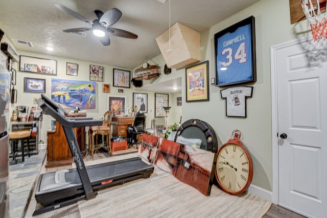 exercise room featuring hardwood / wood-style floors, ceiling fan, and a textured ceiling