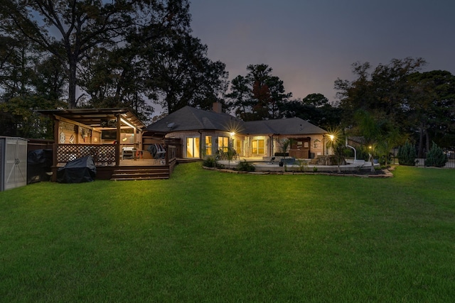 back house at dusk with a lawn, a storage shed, and a wooden deck