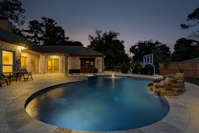 pool at dusk featuring pool water feature and a patio