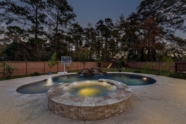 pool at dusk featuring an in ground hot tub and a playground