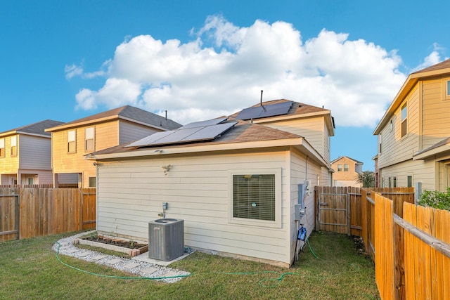 back of property featuring solar panels, central AC, and a lawn