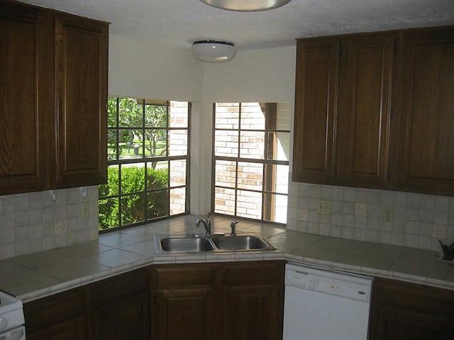 kitchen with dark brown cabinetry, dishwasher, sink, tile countertops, and decorative backsplash