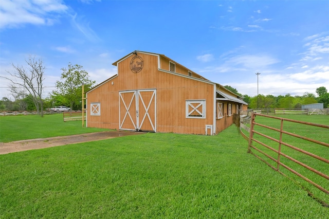 view of barn featuring fence and a lawn