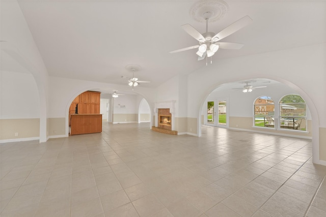 unfurnished living room with lofted ceiling, arched walkways, a lit fireplace, and light tile patterned floors