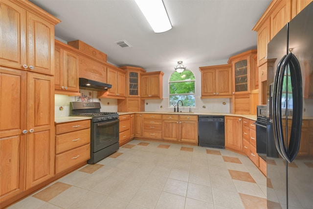 kitchen with under cabinet range hood, a sink, light countertops, black appliances, and tasteful backsplash