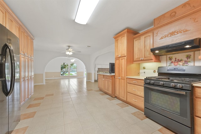 kitchen featuring arched walkways, under cabinet range hood, freestanding refrigerator, tasteful backsplash, and gas stove