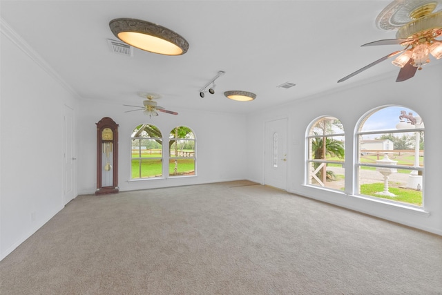 carpeted spare room with ornamental molding, a ceiling fan, visible vents, and track lighting