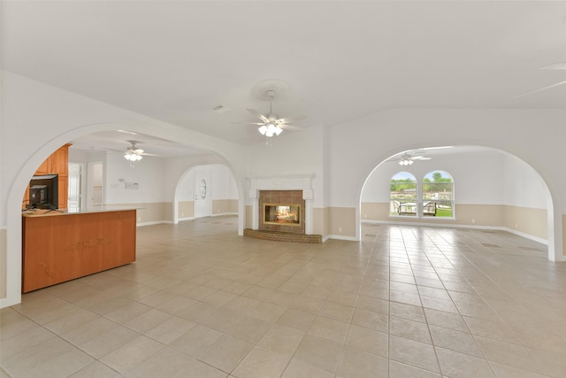 unfurnished living room with light tile patterned floors, arched walkways, a tile fireplace, a ceiling fan, and vaulted ceiling