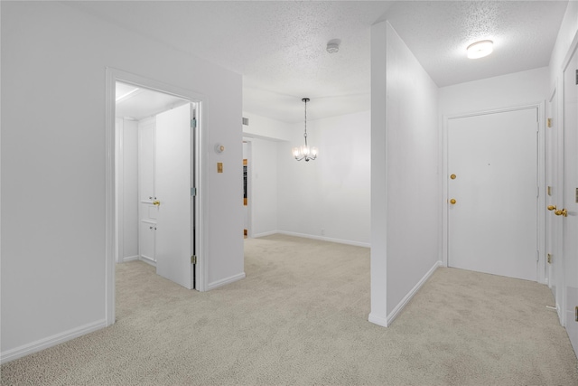 hall with light carpet, a textured ceiling, and an inviting chandelier