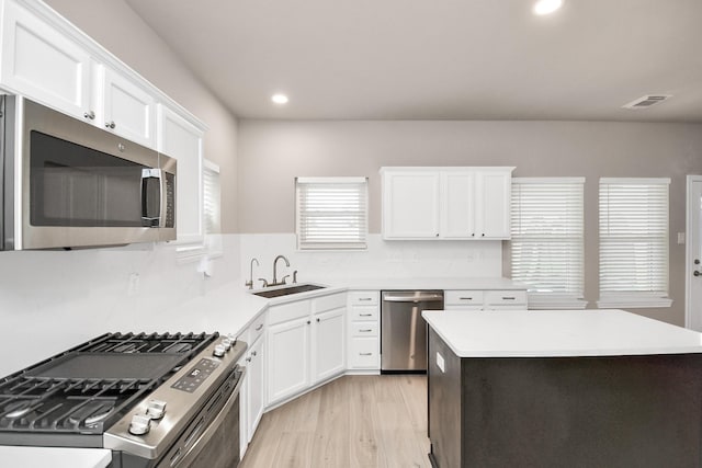 kitchen featuring white cabinets, sink, decorative backsplash, light wood-type flooring, and appliances with stainless steel finishes