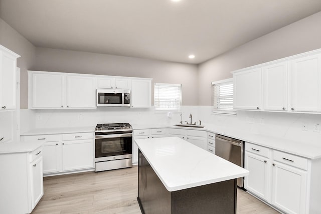 kitchen featuring sink, light wood-type flooring, a kitchen island, white cabinetry, and stainless steel appliances